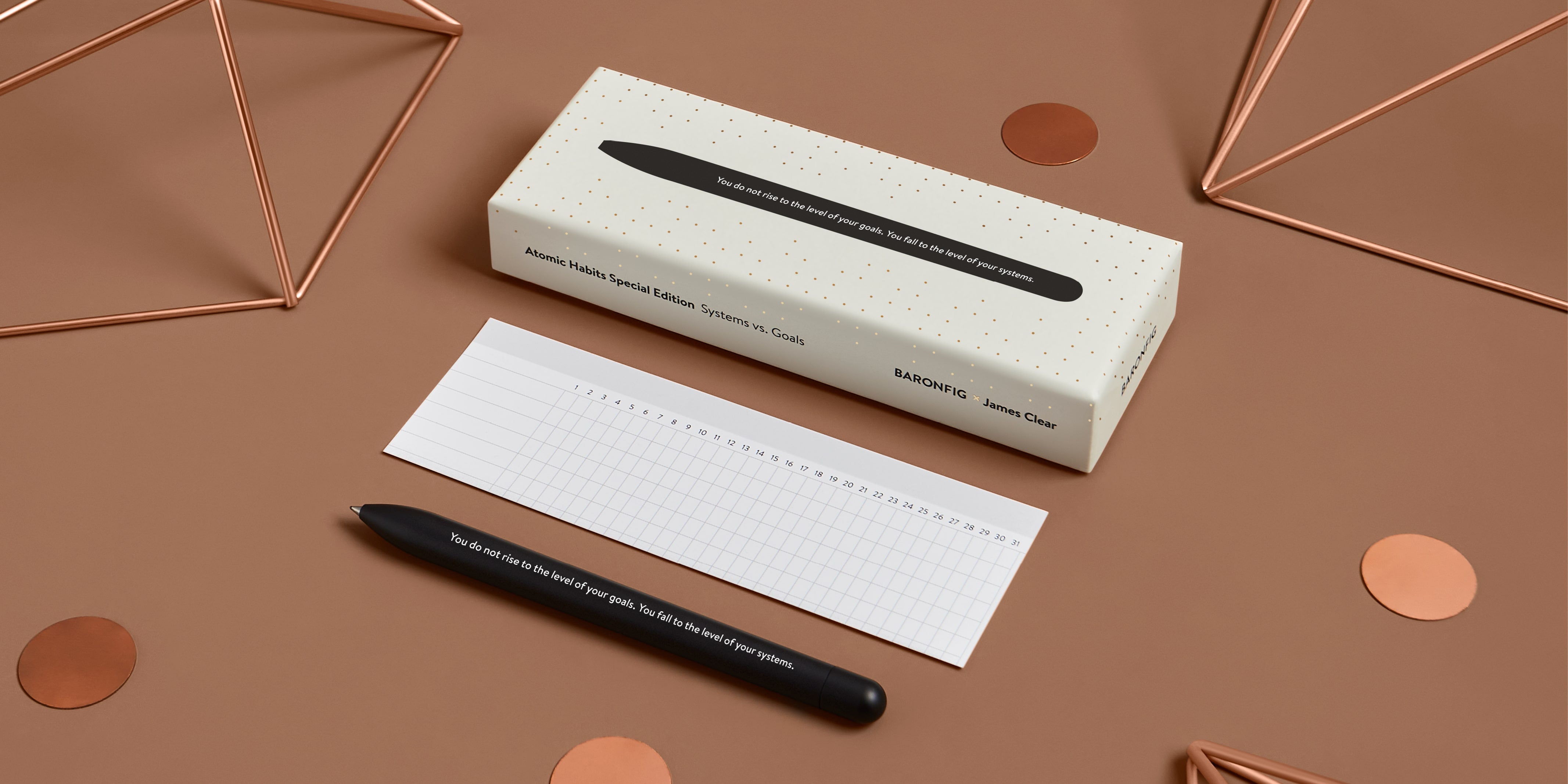 Black Atomic Habits pen and habit tracker insert on a coppor-colored surface with geometric shapes