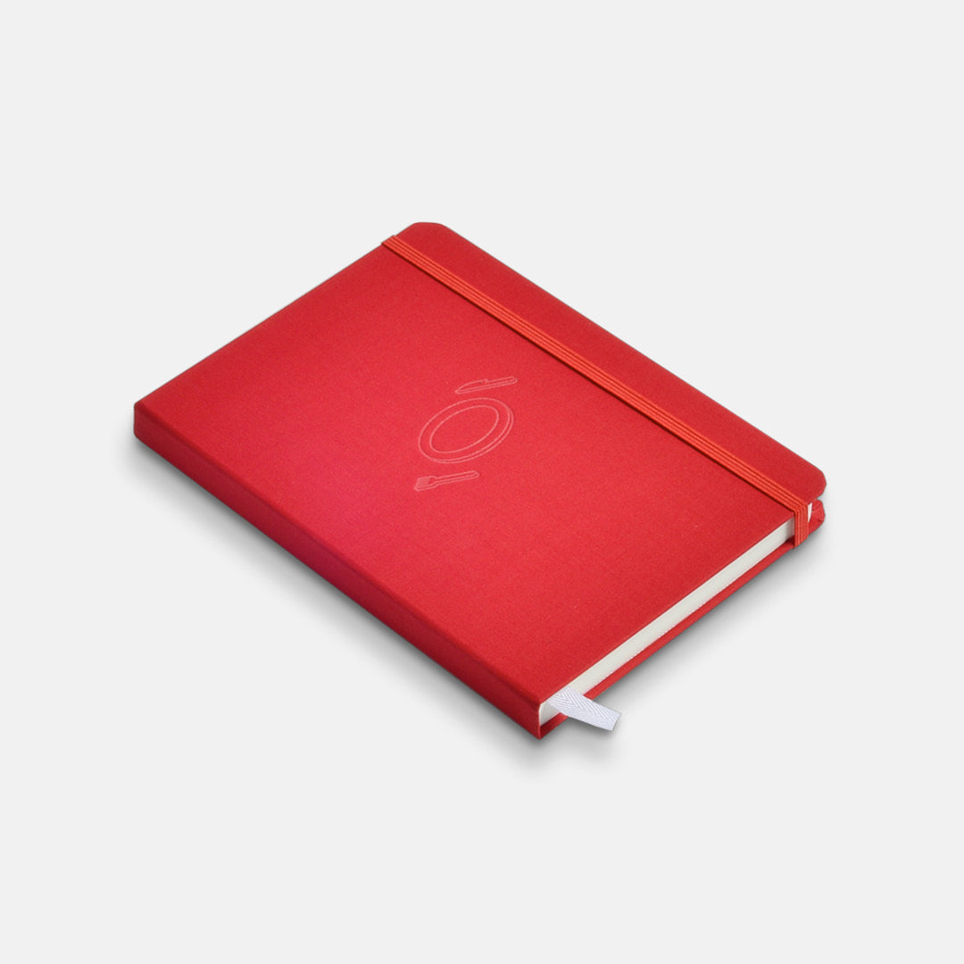 Closed tomato red hardcover Savor Recipe Journal with elastic band closure, cover debossing and white ribbon.